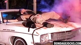 Submissive cop bound on the hood of a car and dominated