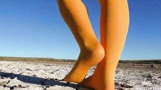 Barefoot walking by dried up lake inside yellow stockings